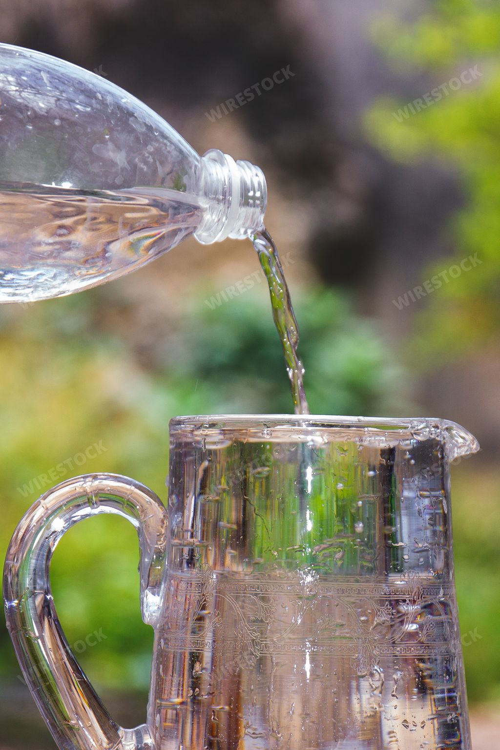 A vertical shot of a plastic bottle pouring water into a glass jug outdoors with blurred background