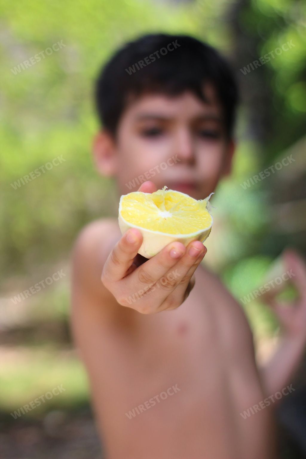 A vertical shot of a Hispanic boy holding and showing a peeled lemon half in his hand