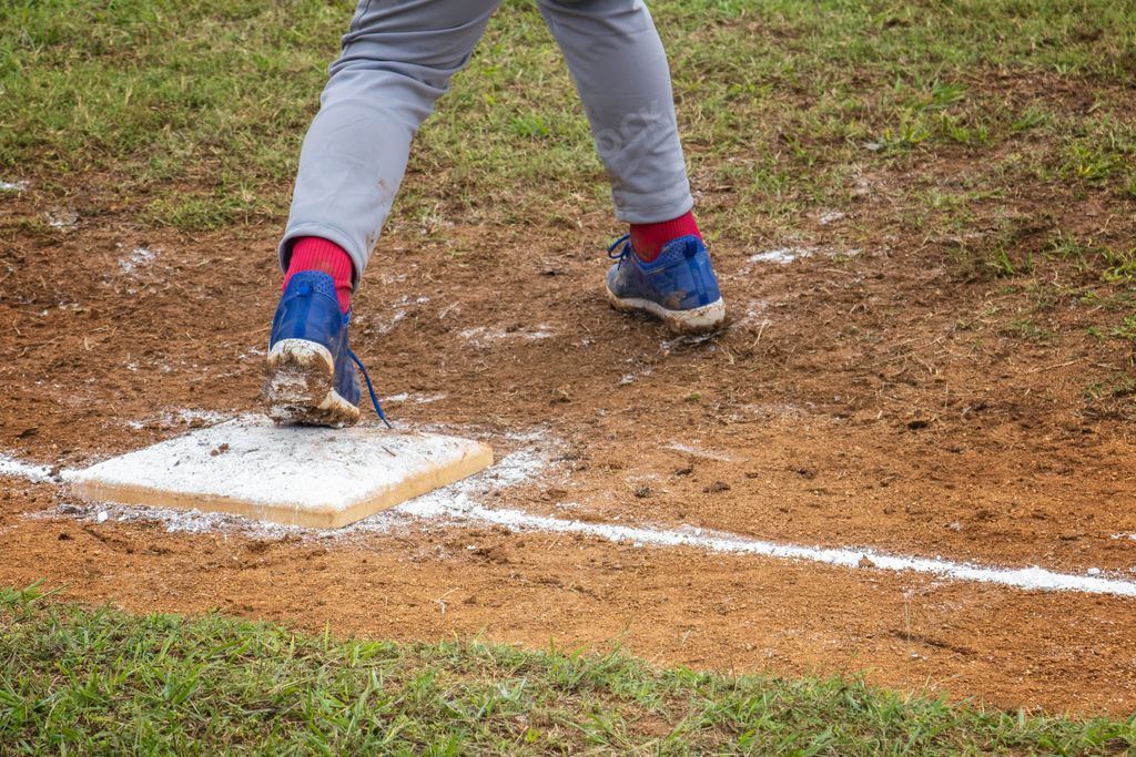 Closeup of an athlete's running shoe with dust and mud-covered spikes on top of a baseball base