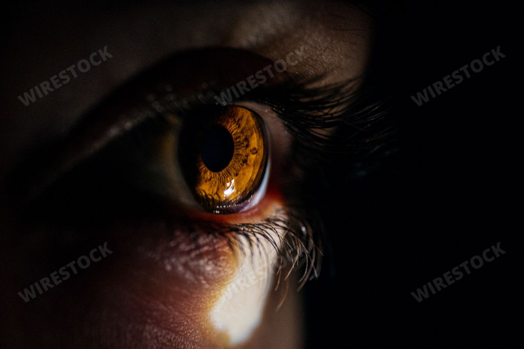 A macro closeup shot of a human eye looking to a small light from a dark room
