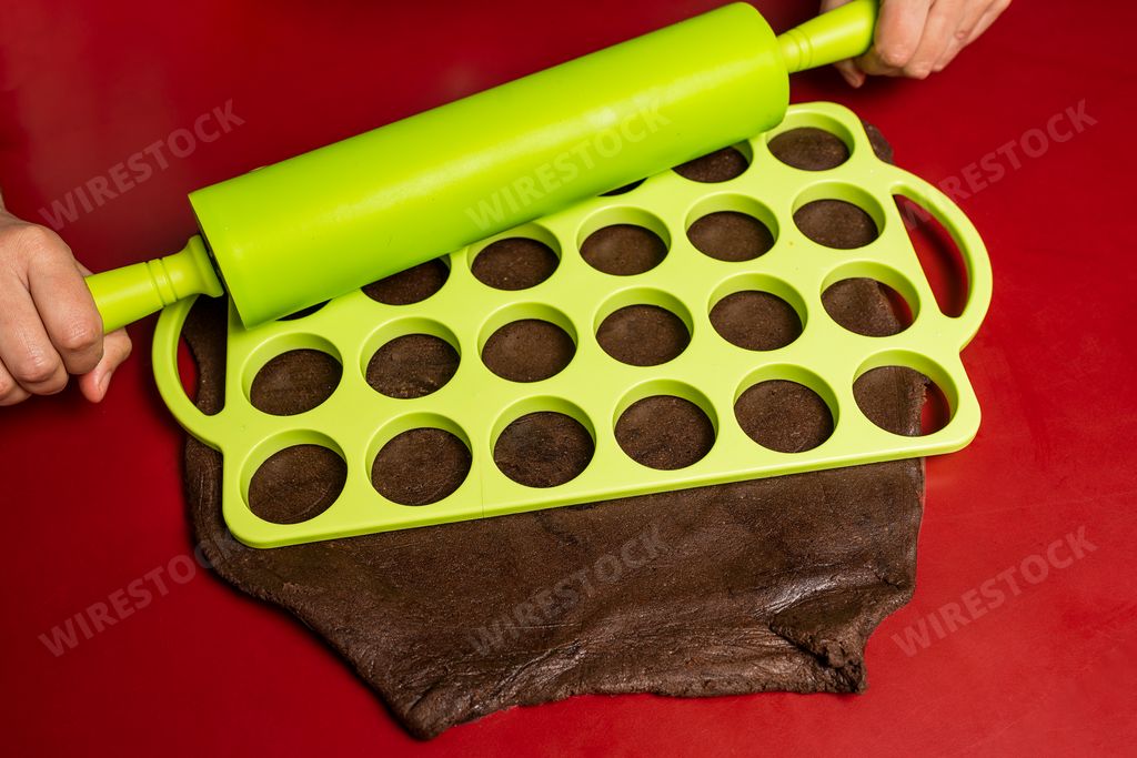 A woman using a rolling pin on a plastic mold to cut cocoa dough to cook Argentinian Alfajores
