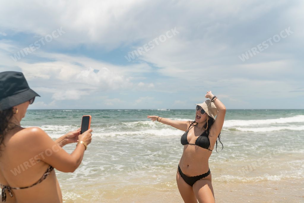 Two young sexy Hispanic girls taking photos of each other at the beach