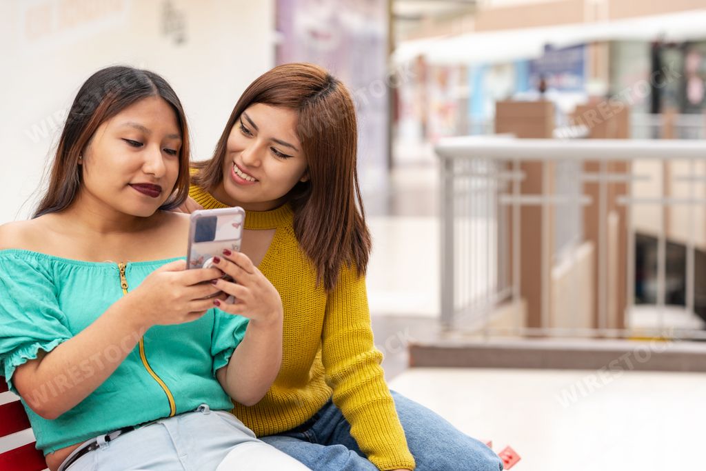 Photo with copy space of two latin women using a mobile in a shopping mall