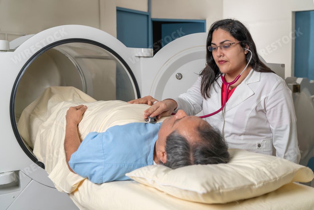 A doctor auscultating a patient on a stretcher in front of a hyperbaric treatment machine