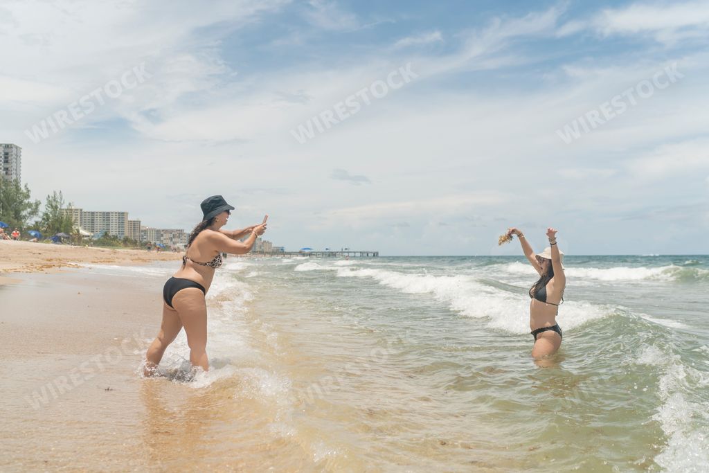 Two young sexy Hispanic girls taking photos of each other at the beach