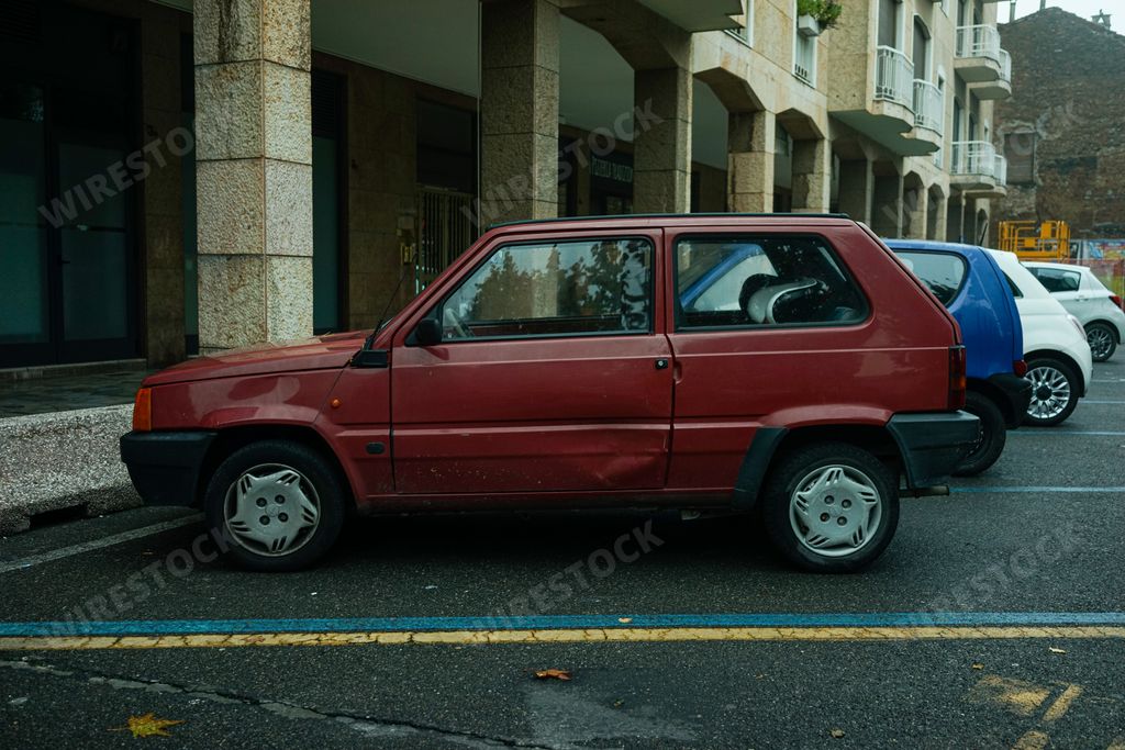 A side view of a Fiat Panda vintage Italian car with a damaged door parked in front of a building