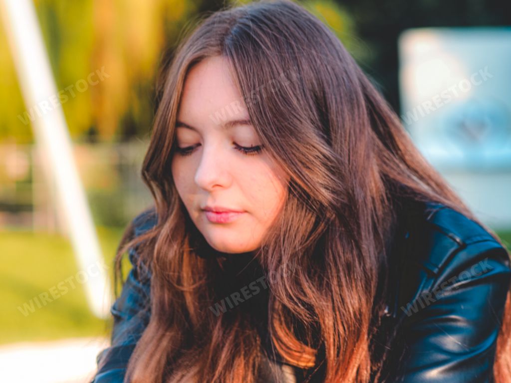 A Caucasian pretty sad girl with a shiny leather jacket, closing eyes with a blurred background