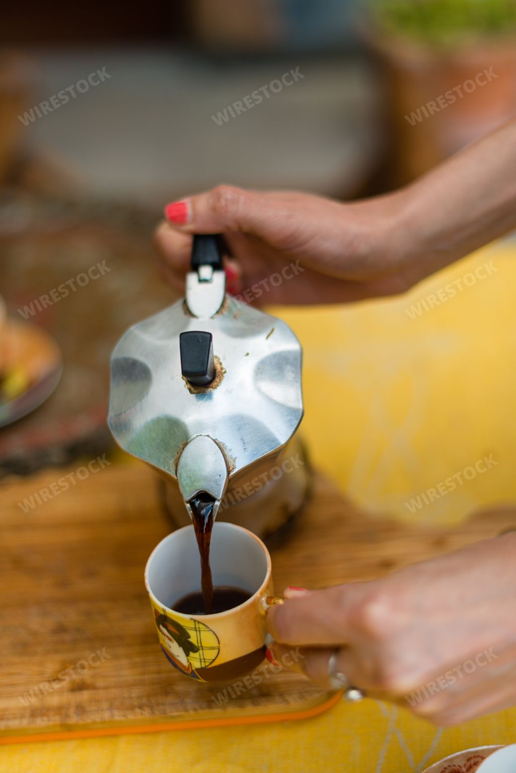 A woman's hand holding metal pot and pouring coffee into a white cup