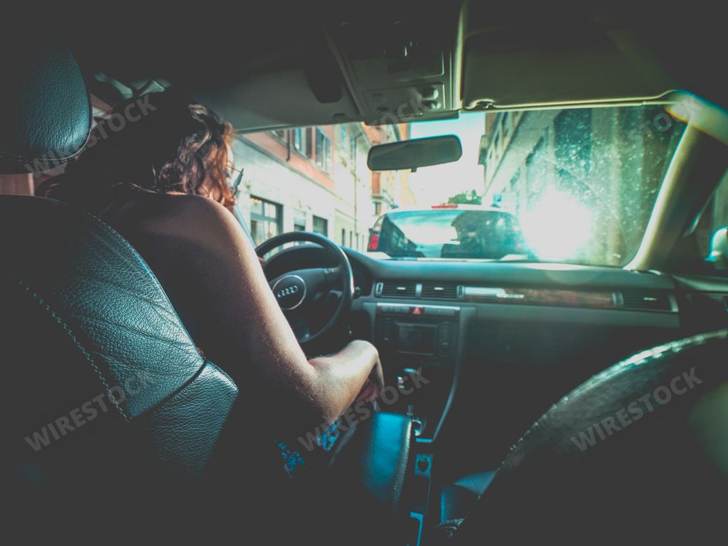 a caucasian female with curly hair inside a car in drivers seat - shot from the back seat