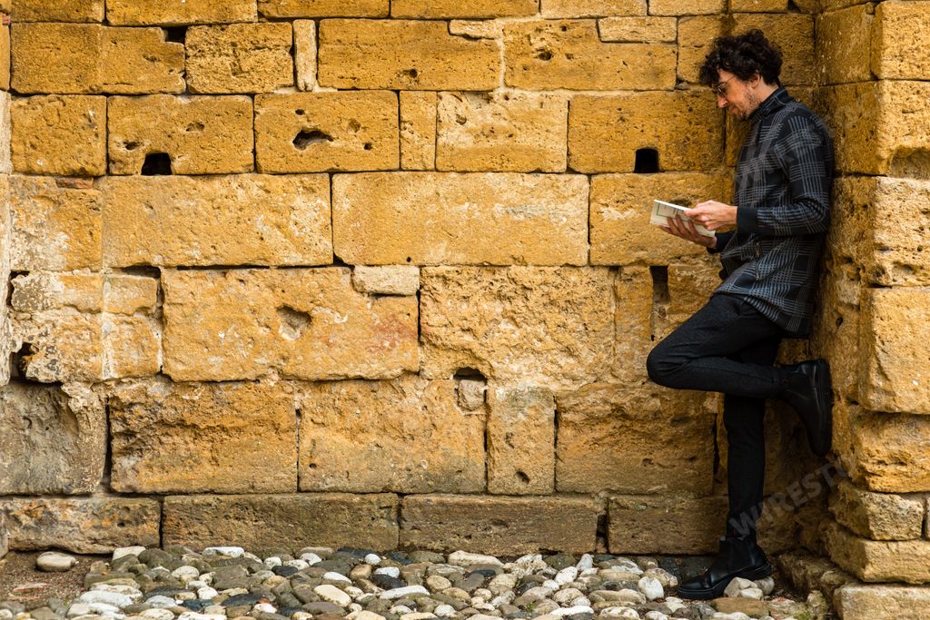 A young Italian man leaning on the wall and reading a book