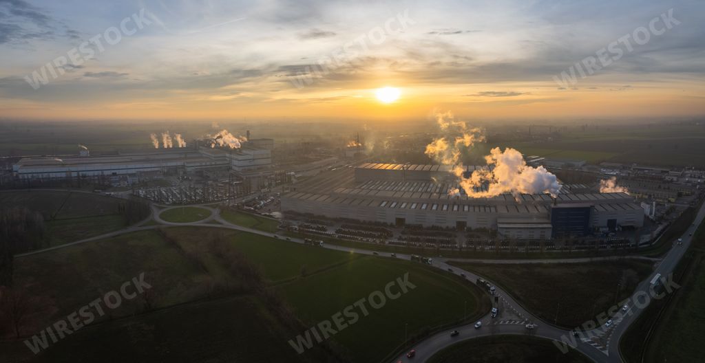Smoke rises from industrial factory chimneys near an empty field