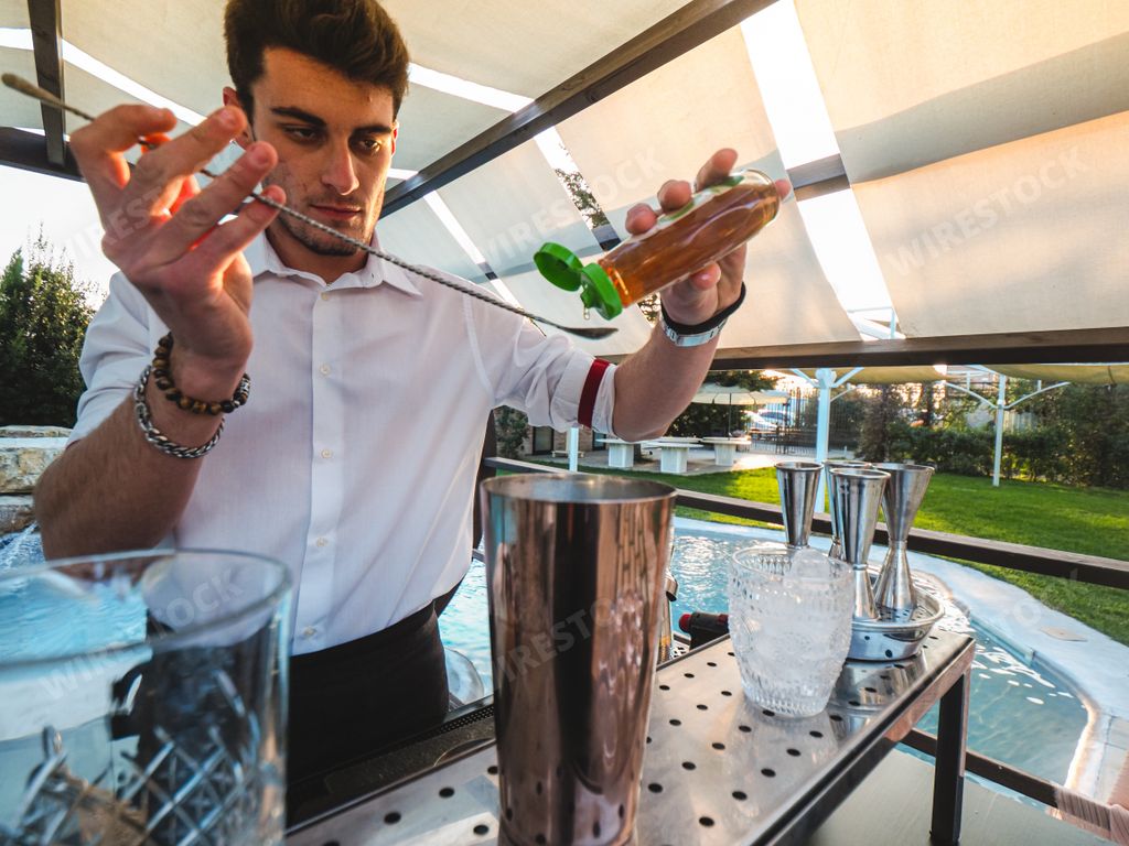 A young Caucasian barman making a refreshing cocktail outdoors at an event