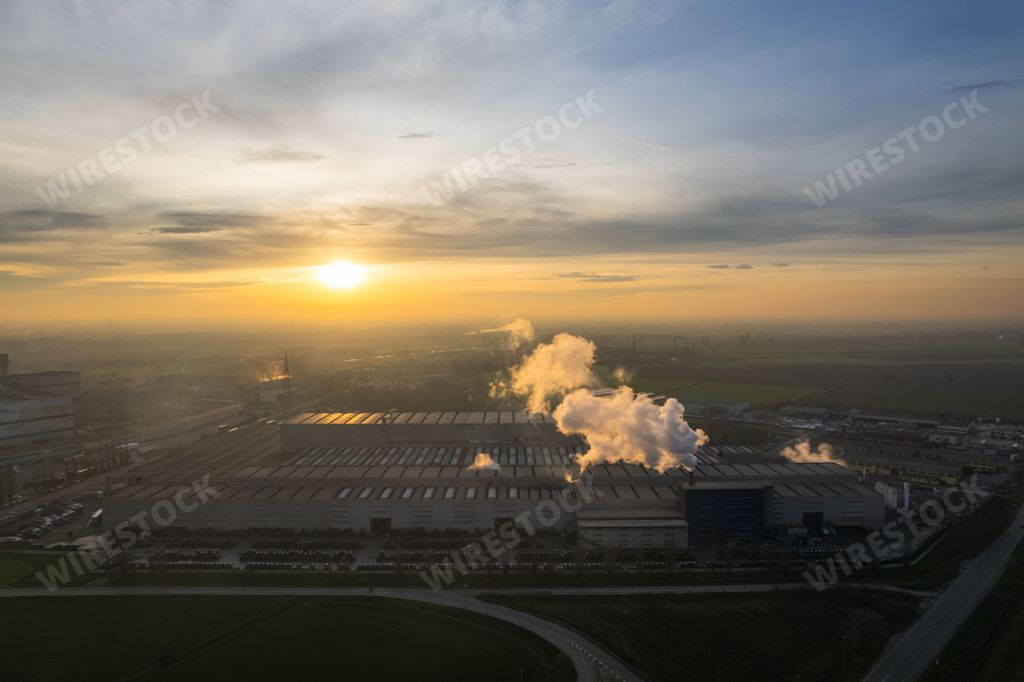 An industrial factory emitting large amounts of smoke into the air in a green field at sunset