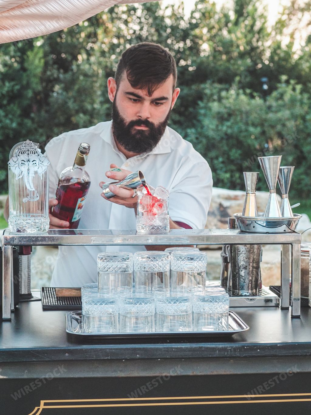 A young Caucasian barman making refreshing cocktails outdoors at a private luxury event