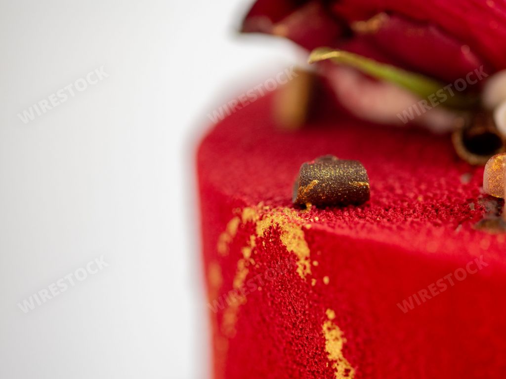 A macro shot of the edge of a red cake decorated with golden edible dye and chocolate
