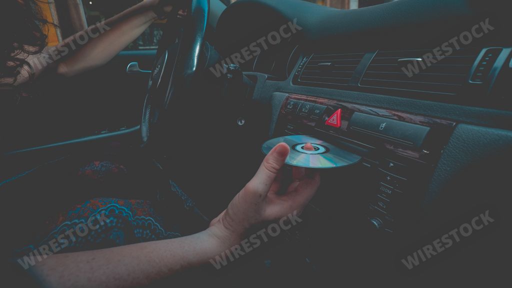 a caucasian female with curly hair inside a car putting an optical disc into a player