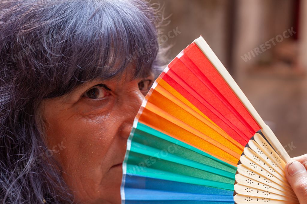 A Hispanic senior female posing with a hand fan with the LGBT flag colors
