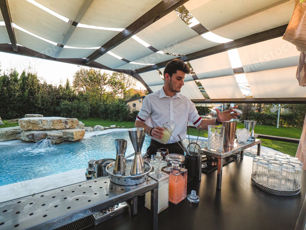 A young Caucasian barman making a refreshing cocktail outdoors by the pool at an event