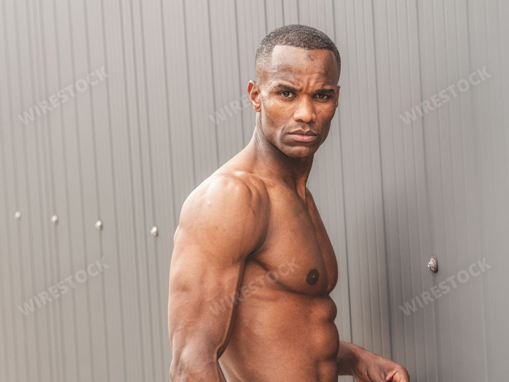 A portrait of a handsome shirtless man demonstrating perfect torso in the gray wall background