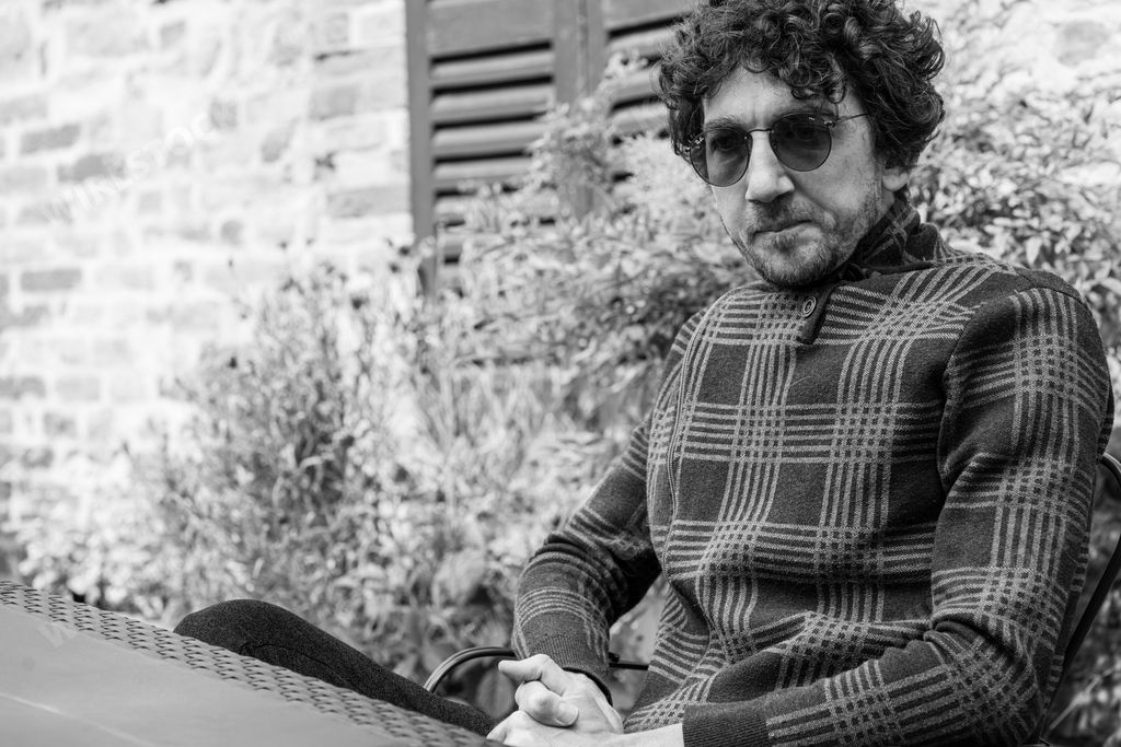 A grayscale shot of a young Italian man with curly hair and sunglasses