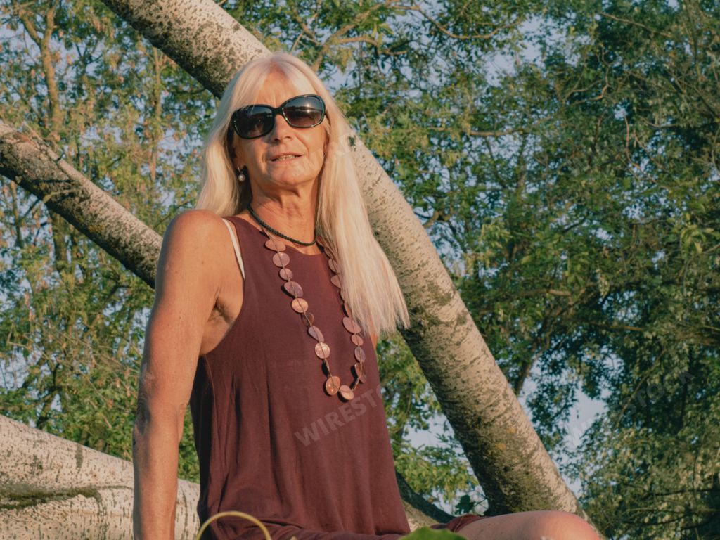 tall fit caucasian adult blonde woman in a park near a big fallen tree. Outdoor portrait of positive confident mature woman.