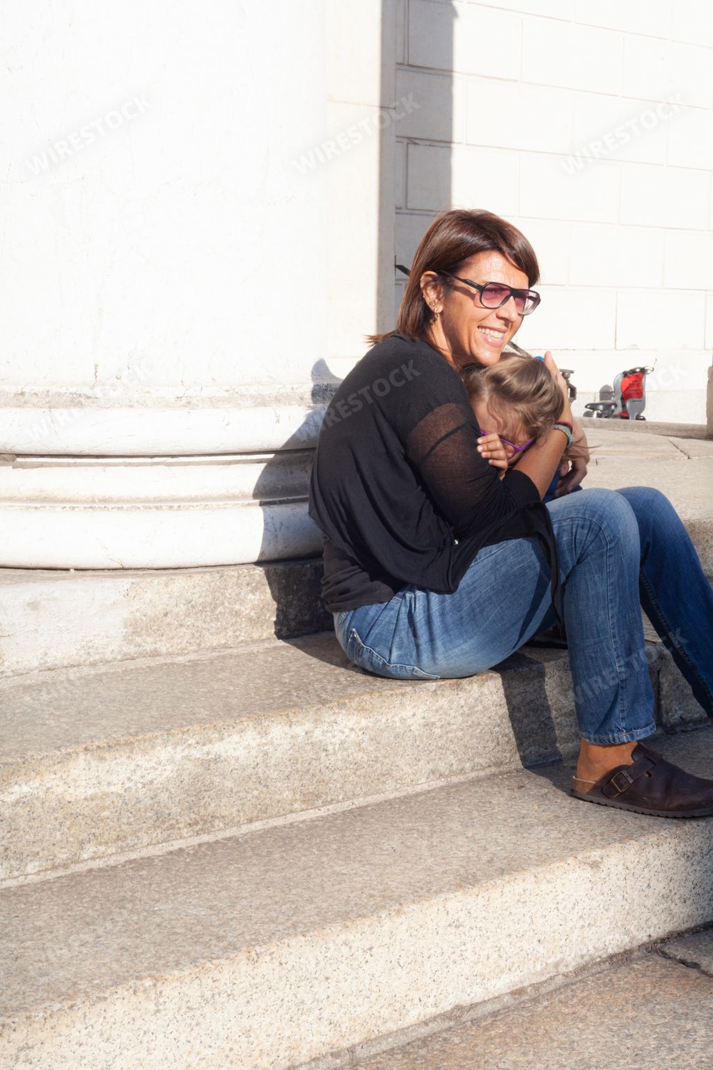 A young smiling mother sitting on stairs and hugging her little daughter