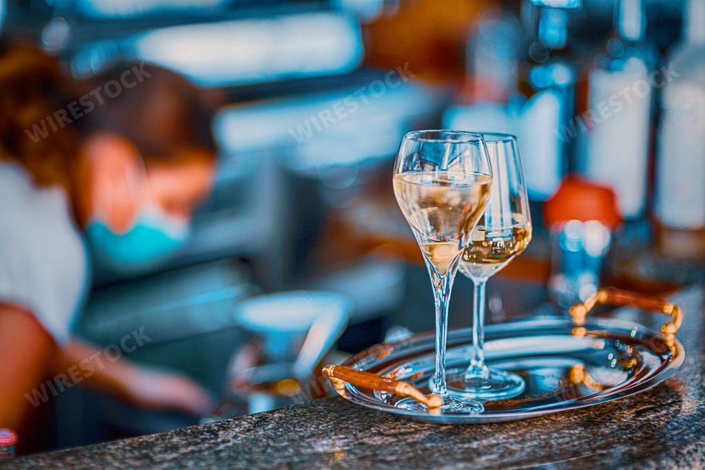 A young female bartender wearing face mask pouring sparkling white