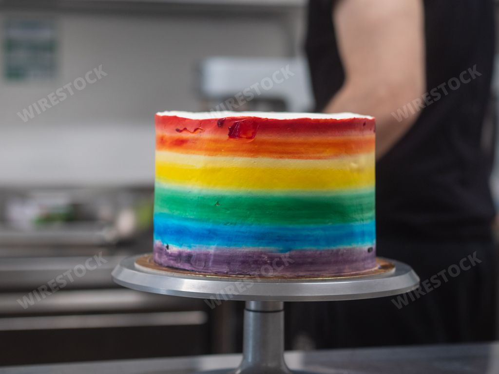 A colorful rainbow cake displayed on a cake stand with vibrant frosting in a rainbow gradient pattern