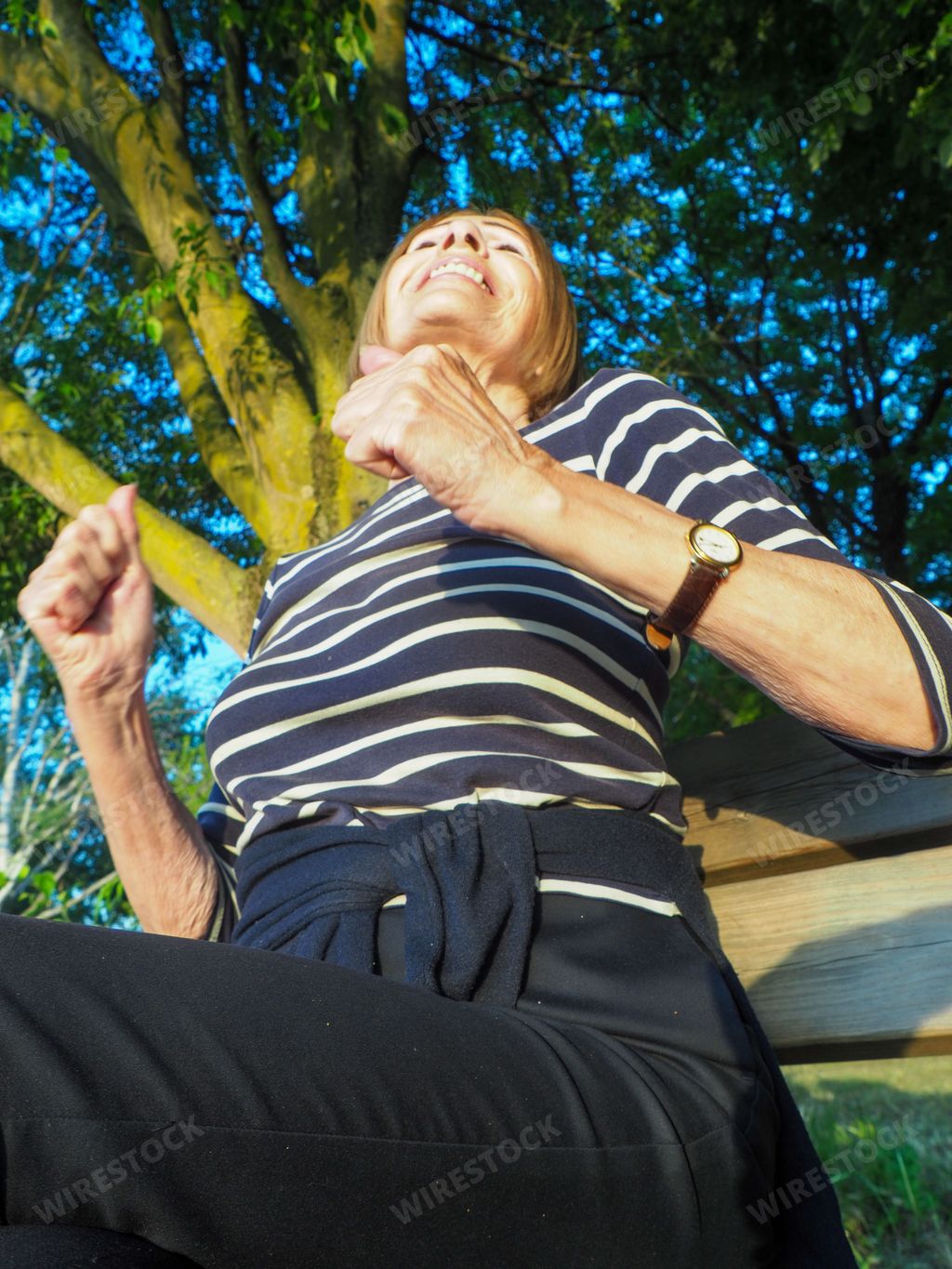adult mature caucasian woman relaxing sitting on a bench in a park bench with legs crossed in springtime