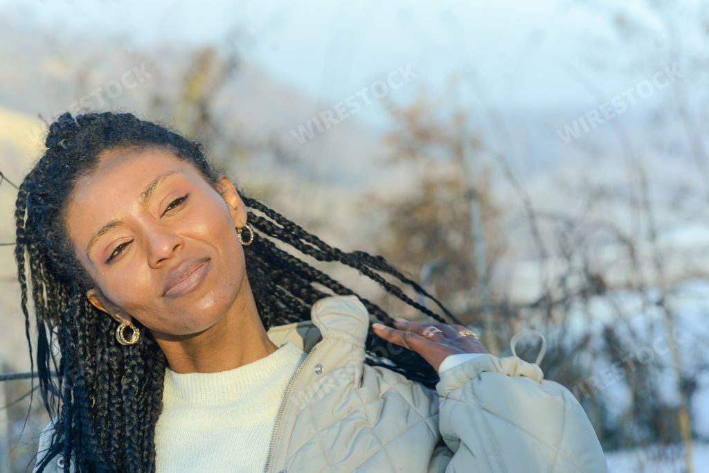 An African-American woman with black braided hair smiling in a blurry background