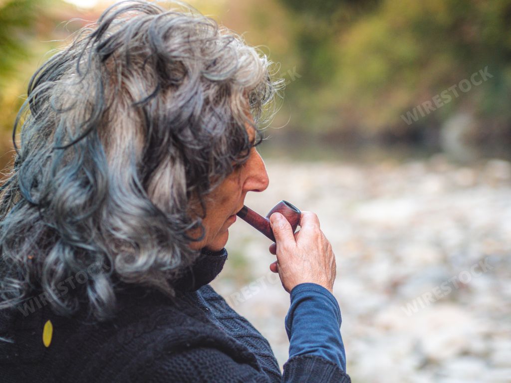 A portrait of a thoughtful older woman sitting in the park and smoking pipe