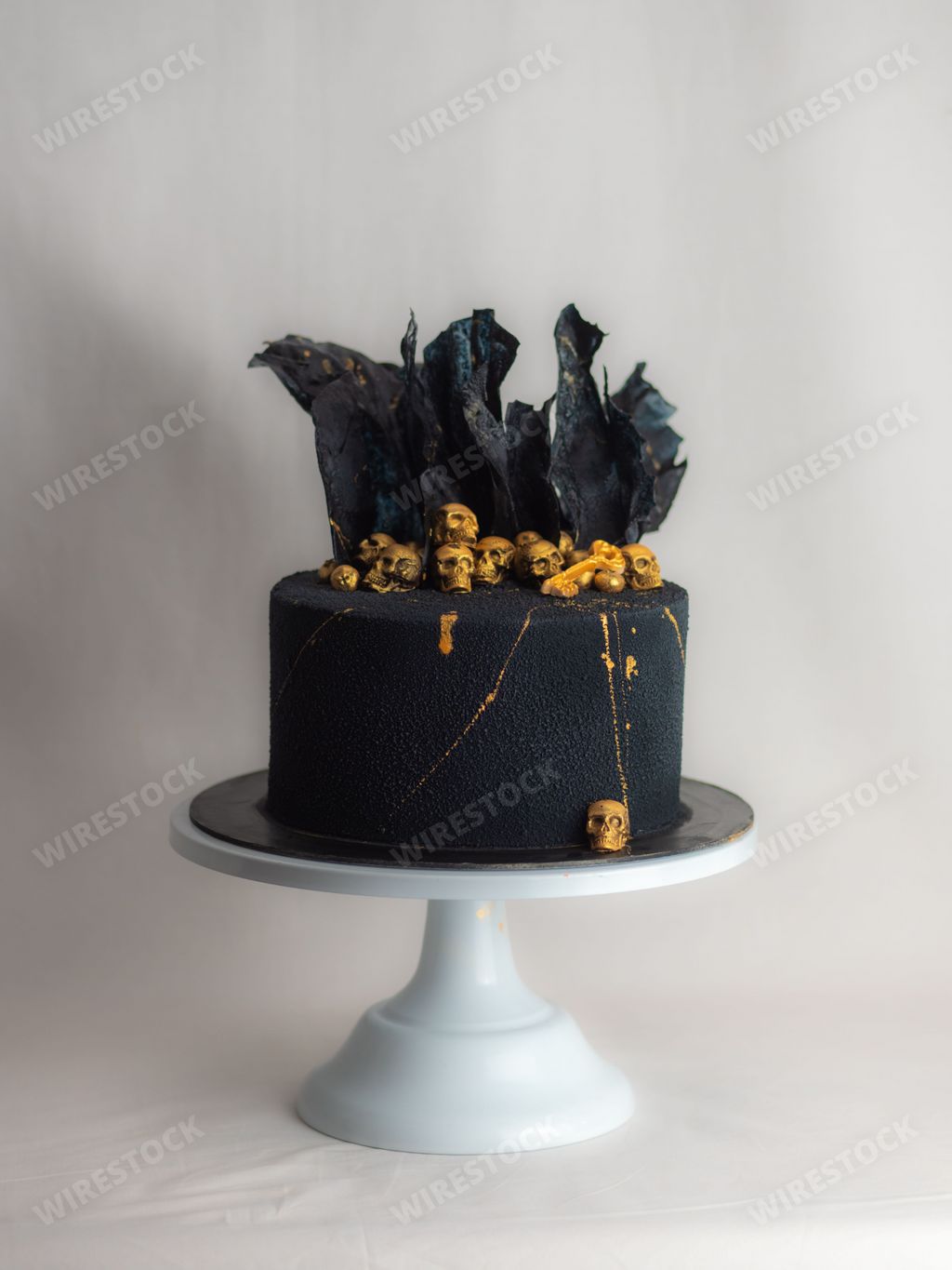 A black birthday cake decorated with golden skulls and black rice paper sails.