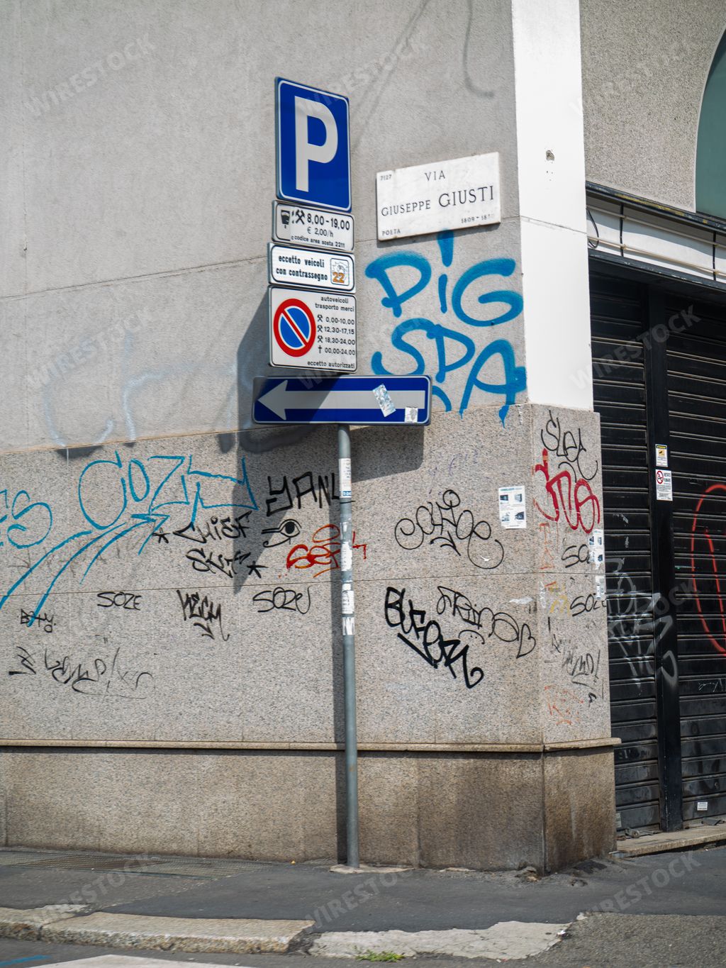 A vertical shot of road signs and writings on the wall in a street in Milan, Italy