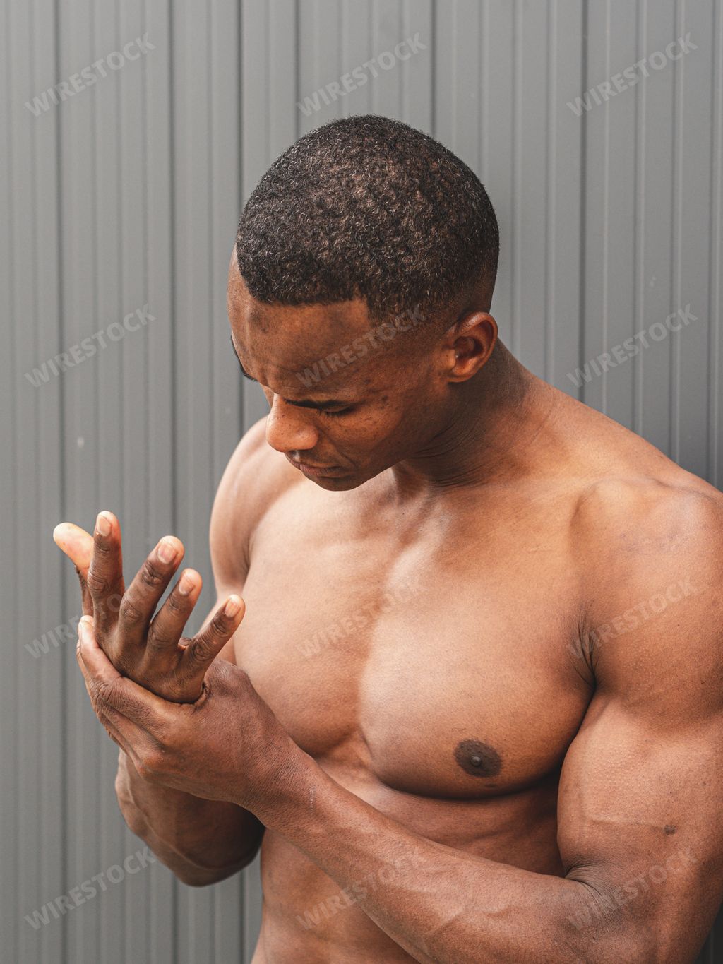 A muscular African man is posing shirtless and curiously watching his hand