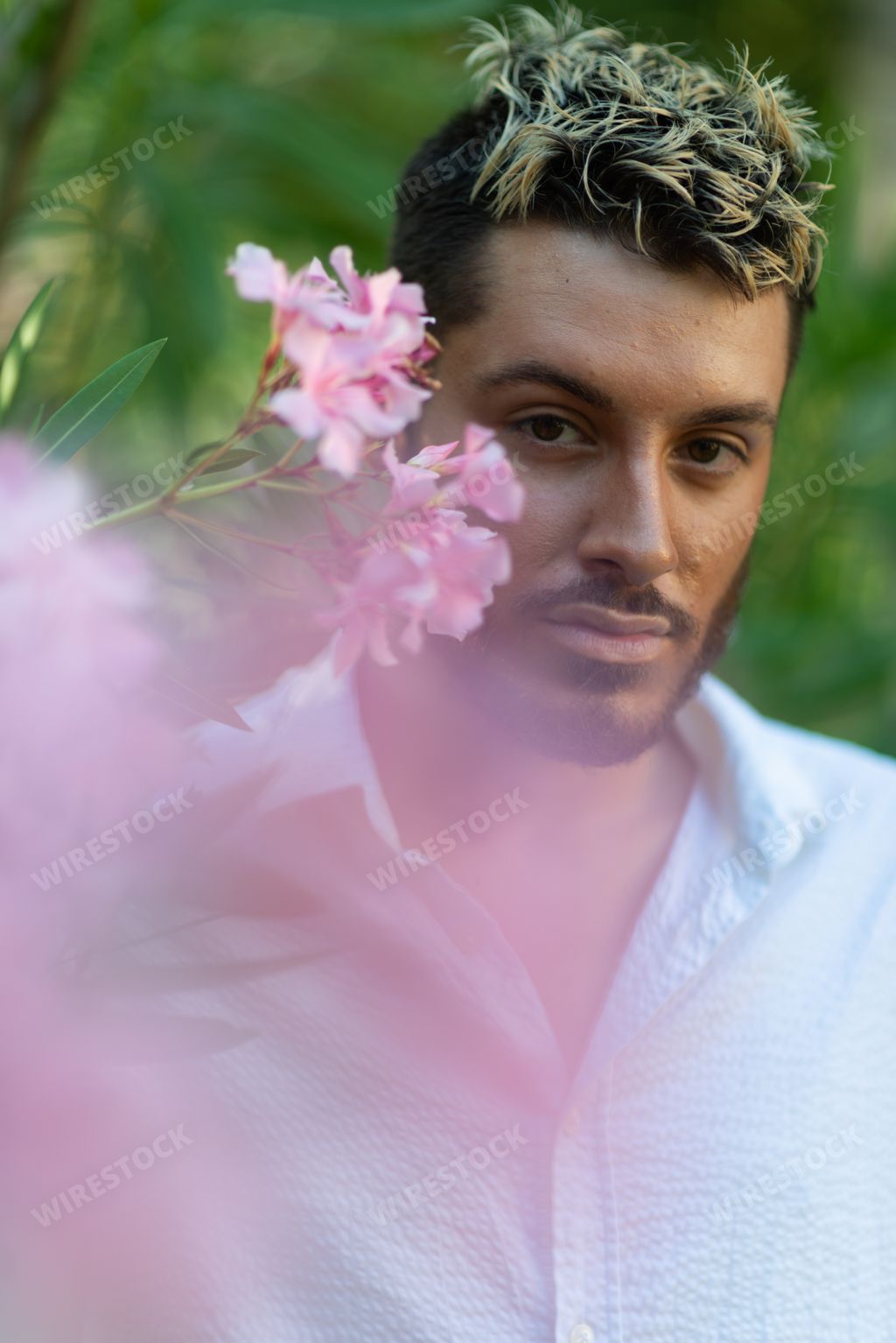 A vertical shot of a young attractive Caucasian guy with ombre hair from Italy in an oleander garden