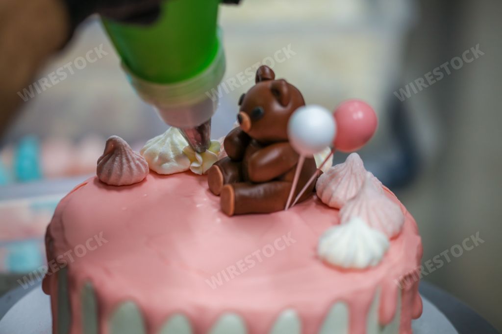 Adorable brown teddy bear perched atop a beautiful pink frosted cake, with a festive purple bow