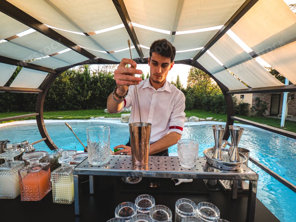 A young Caucasian barman making a refreshing cocktail outdoors by the pool at an event