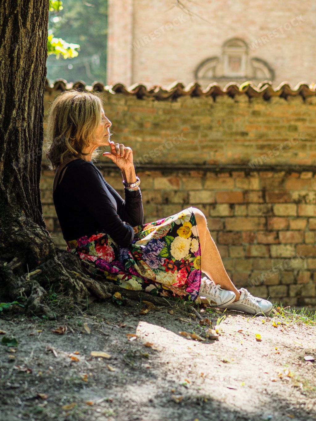 A vertical shot of beautiful elderly Caucasian woman sitting under a tree in daytime