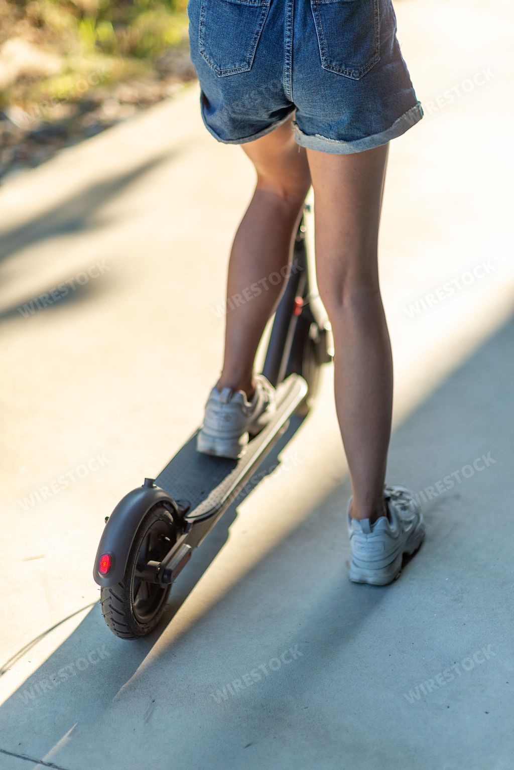 A vertical shot of a sexy woman riding an electric scooter on a summer day