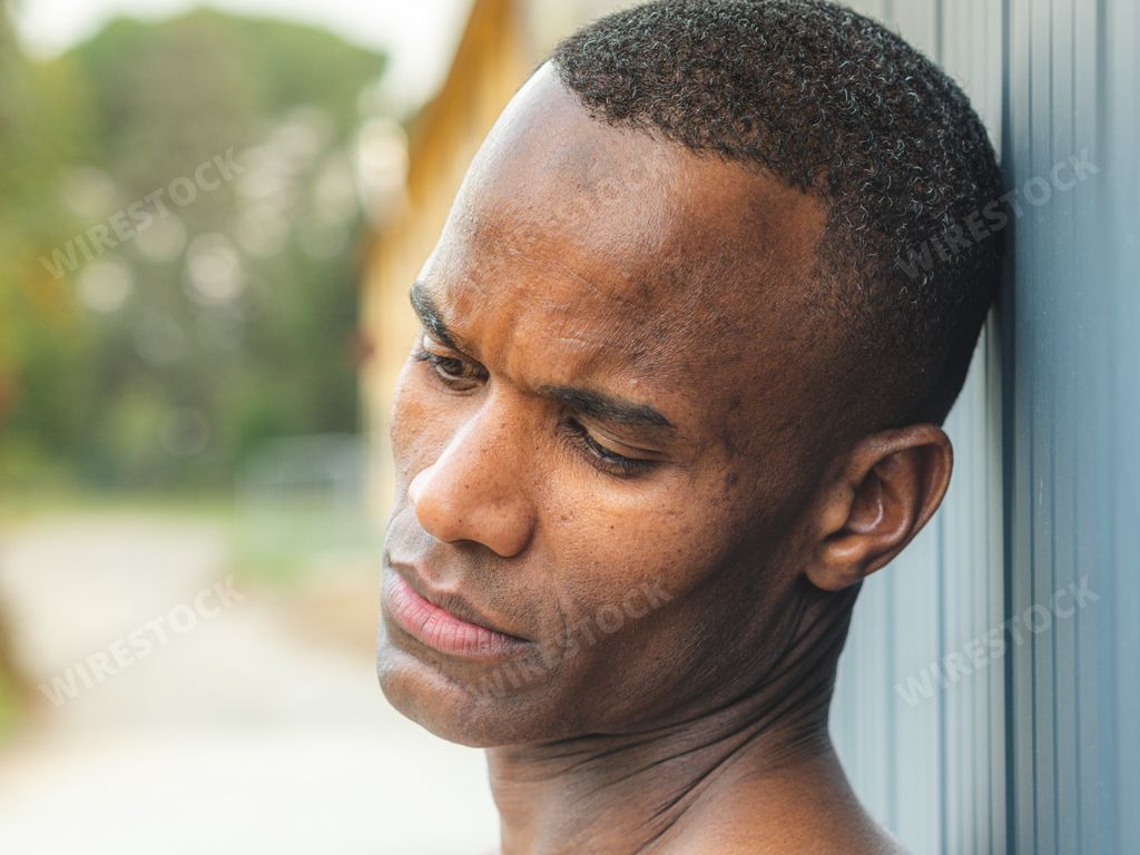 A portrait of a brooding African man leaning his head on the wall