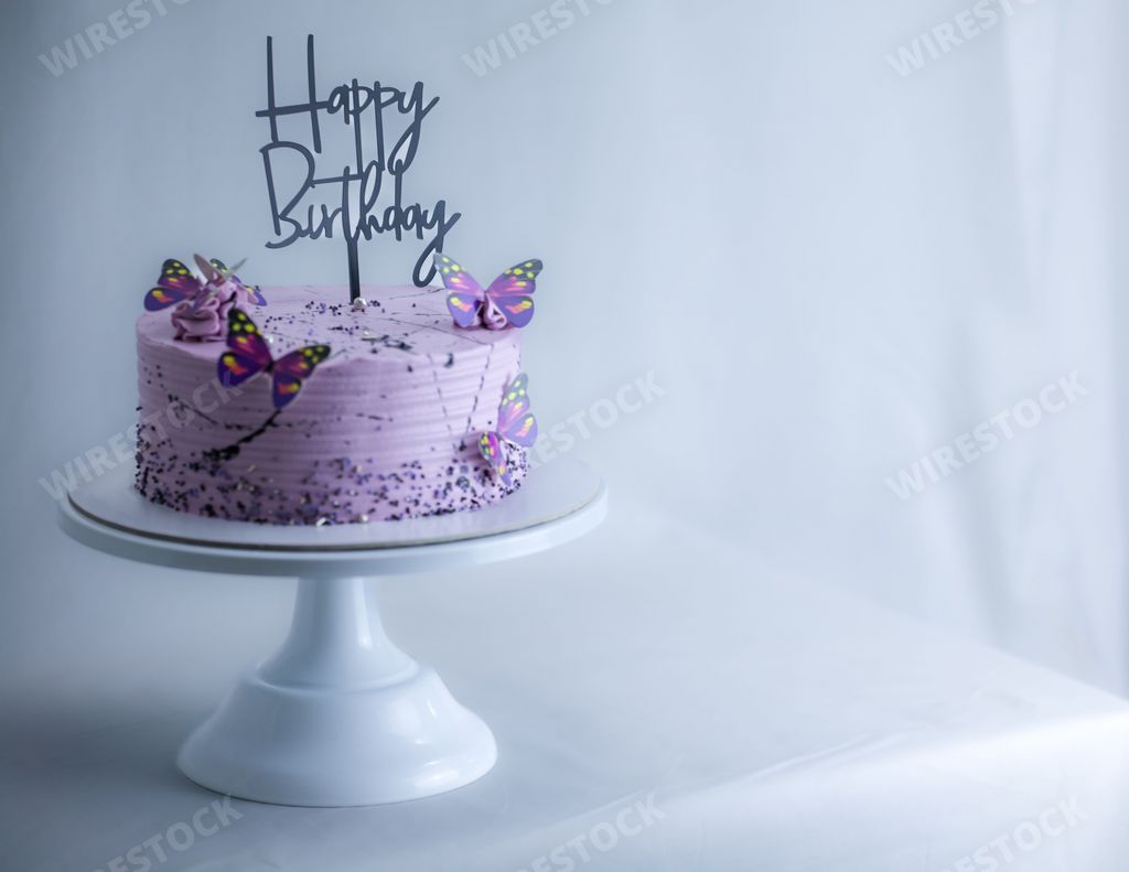 A frosted layered icing lilac cake with a happy birthday sign and butterflies