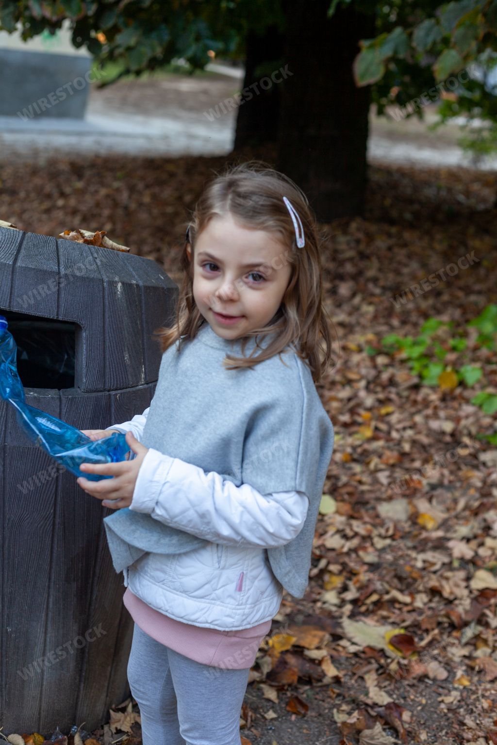 A little blonde Caucasian girl throwing plastic into a recycle bin