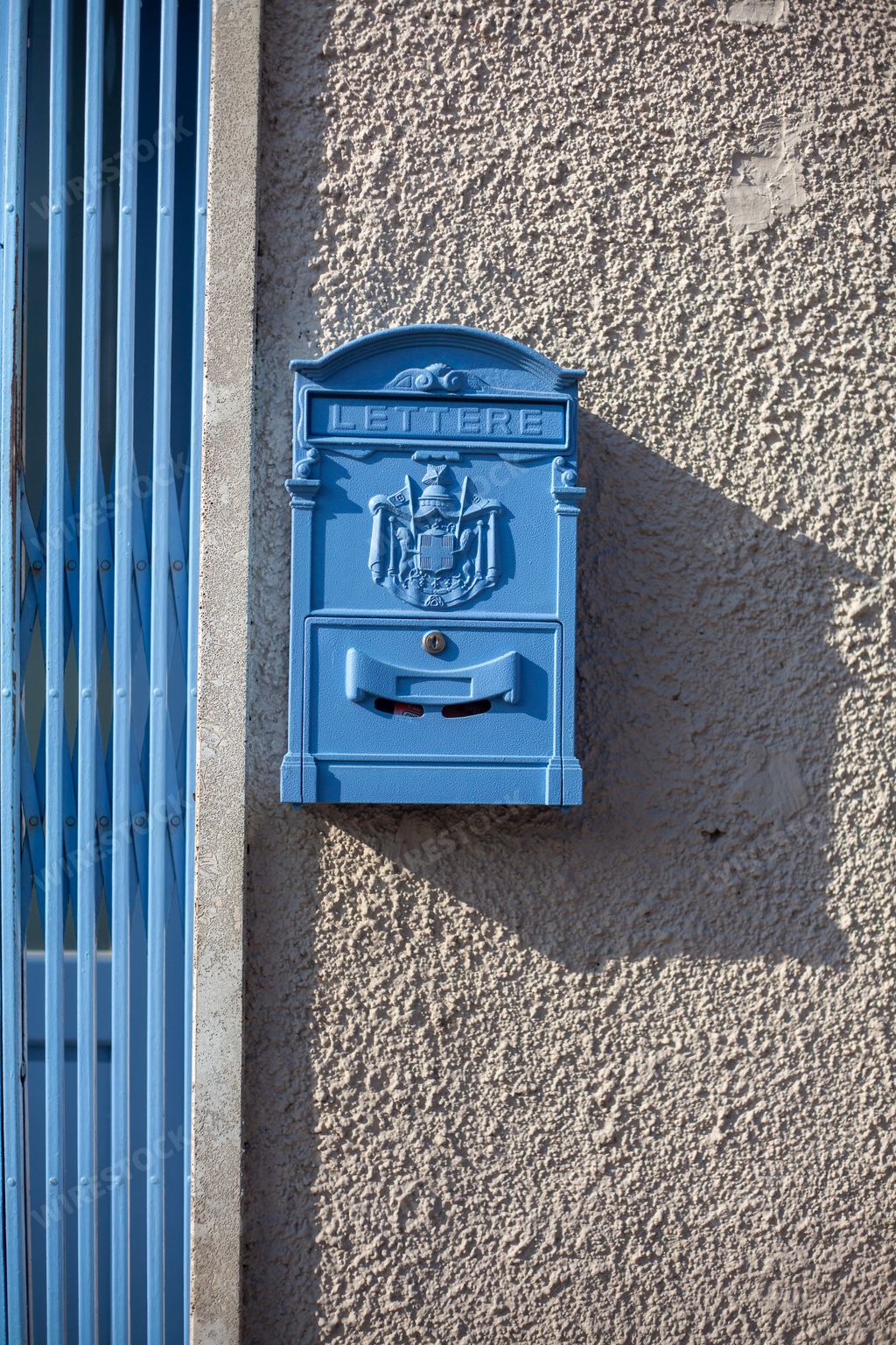 A vertical shot of a cute, small, blue mailbox on the wall in Annico, Italy