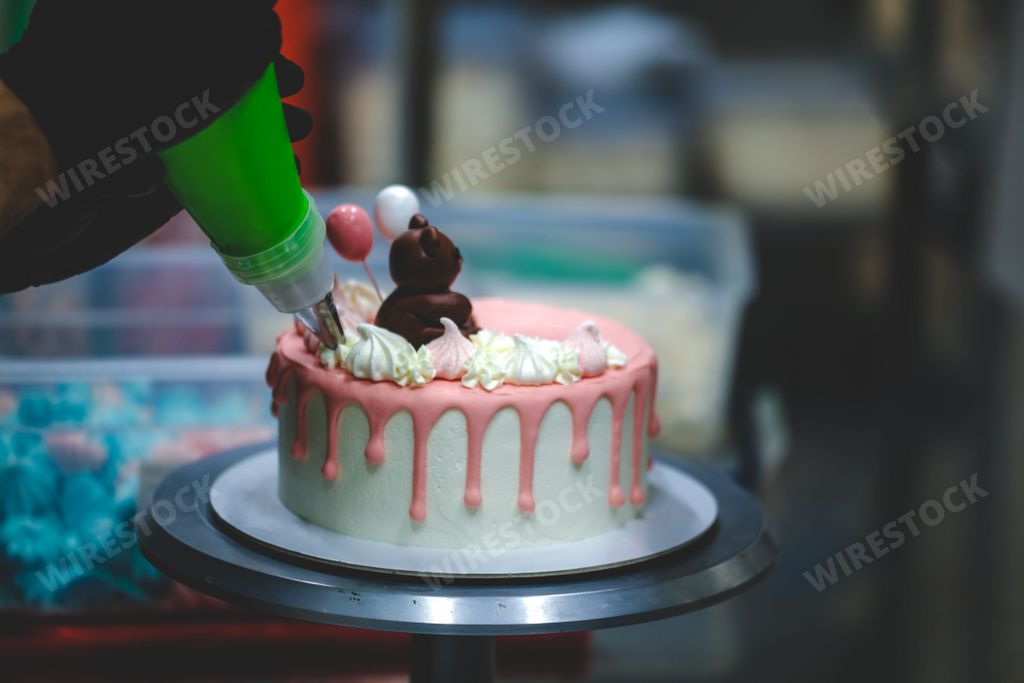 The process of cake baking with the chef decorating the frosted cake with dripping cream and a cute bear