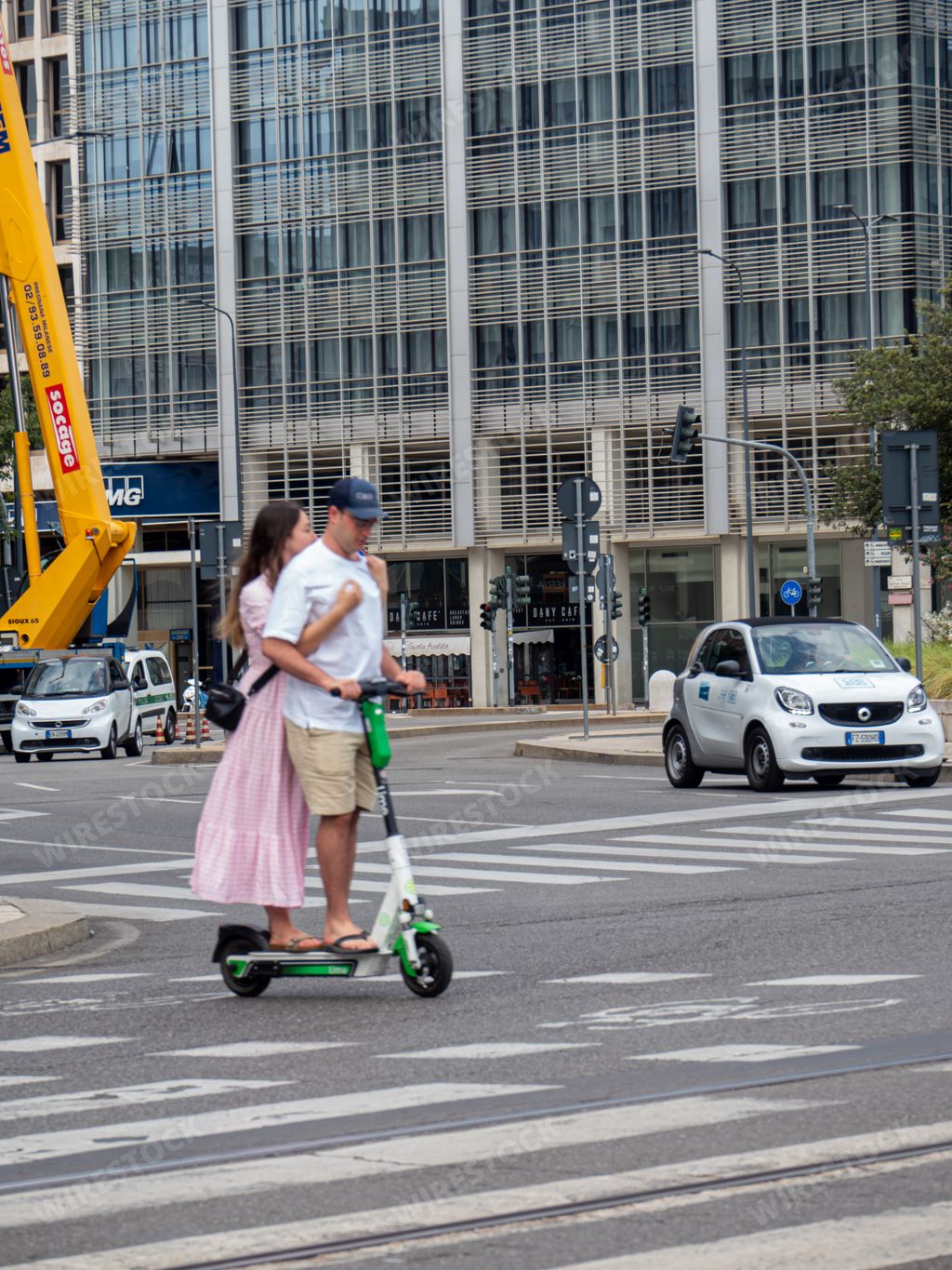 A vertical shot of a couple riding on a Lime electric scooter in Milan, Italy