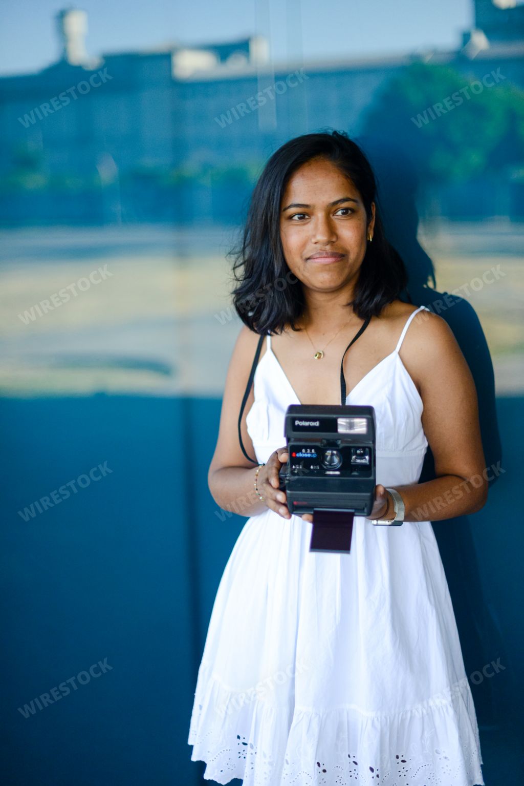 a vertical shot of a south asian female with polaroid vintage instant camera on blue background