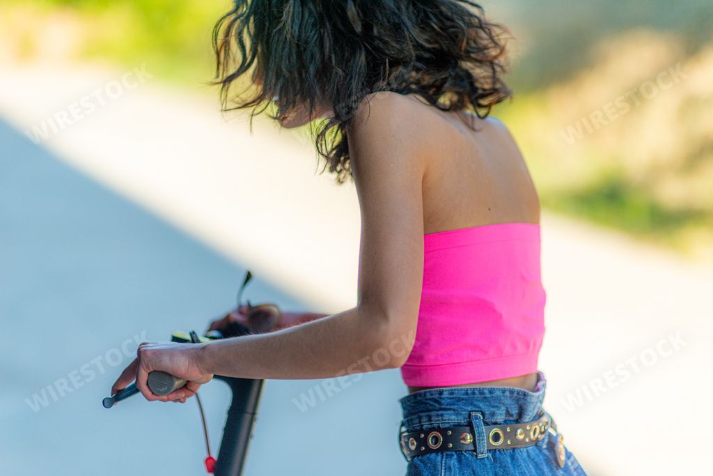 A sexy woman in pink tube riding an electric scooter on a summer day