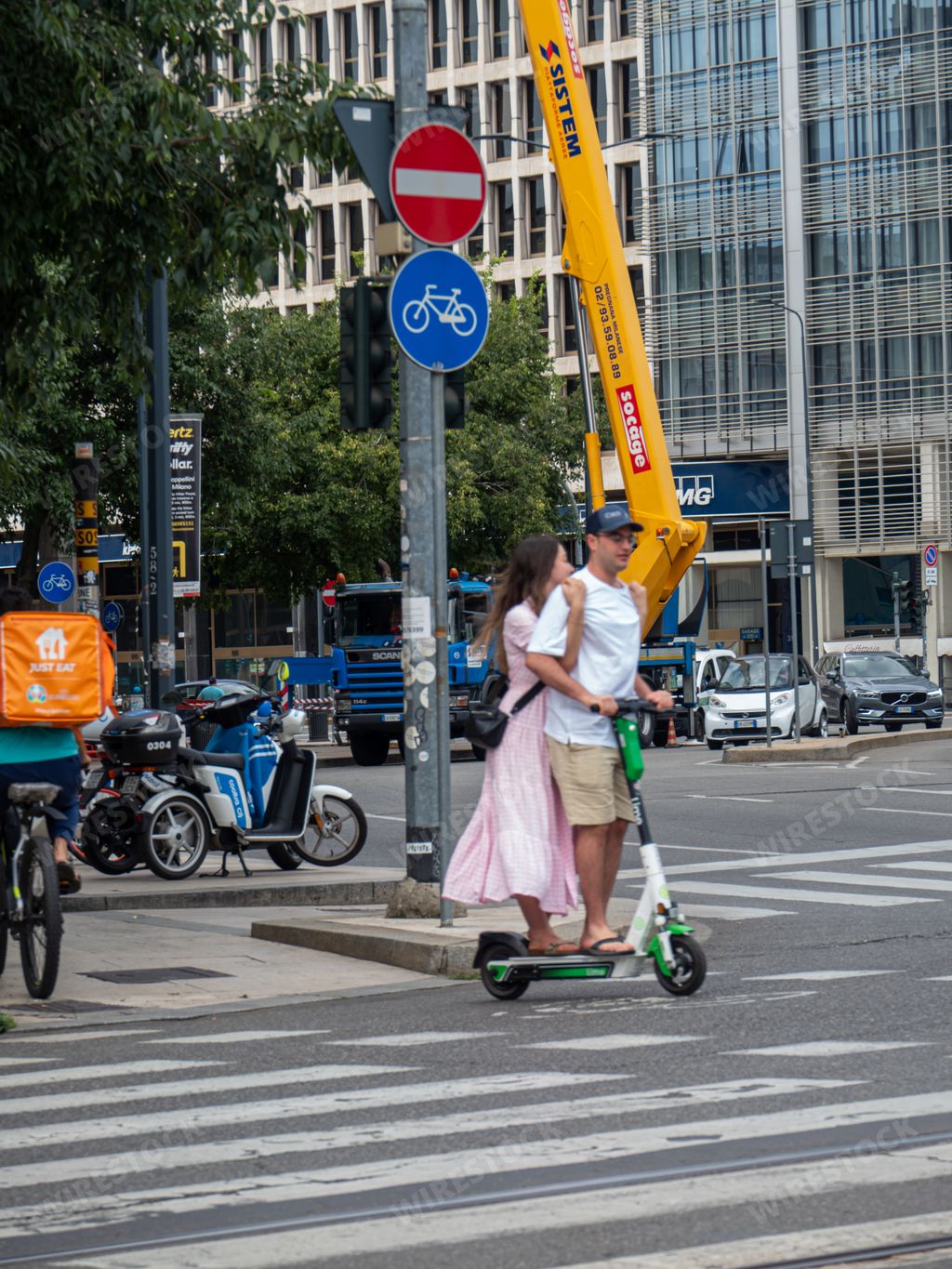A vertical shot of a couple riding on a Lime electric scooter in Milan, Italy