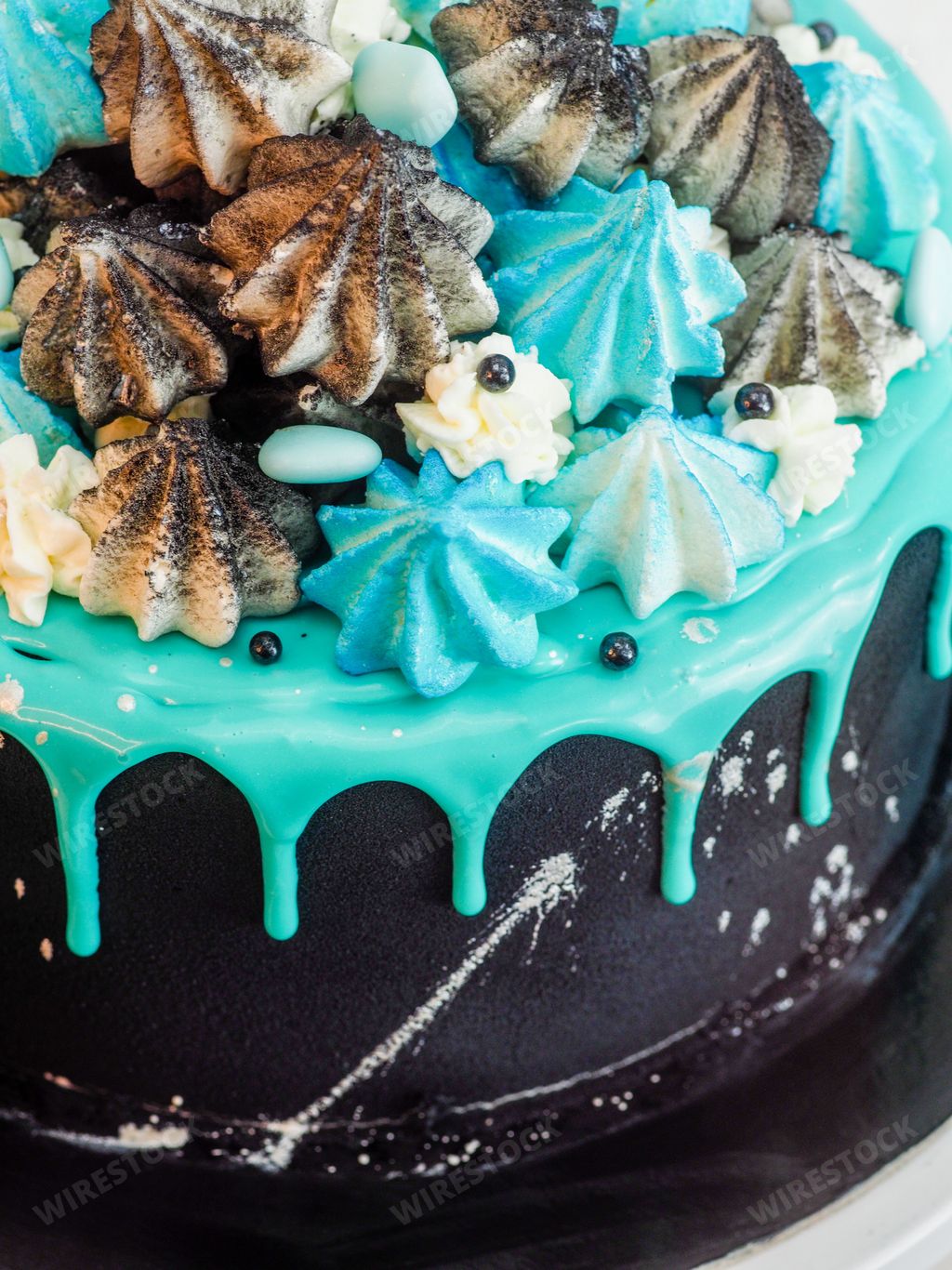 A closeup of a delicious black cake decorated with blue frost and colorful meringues