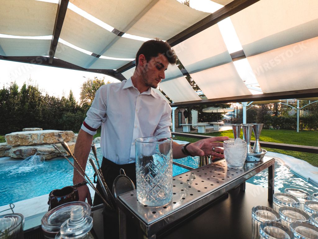 A young Caucasian barman making a refreshing cocktail outdoors by the pool at an event